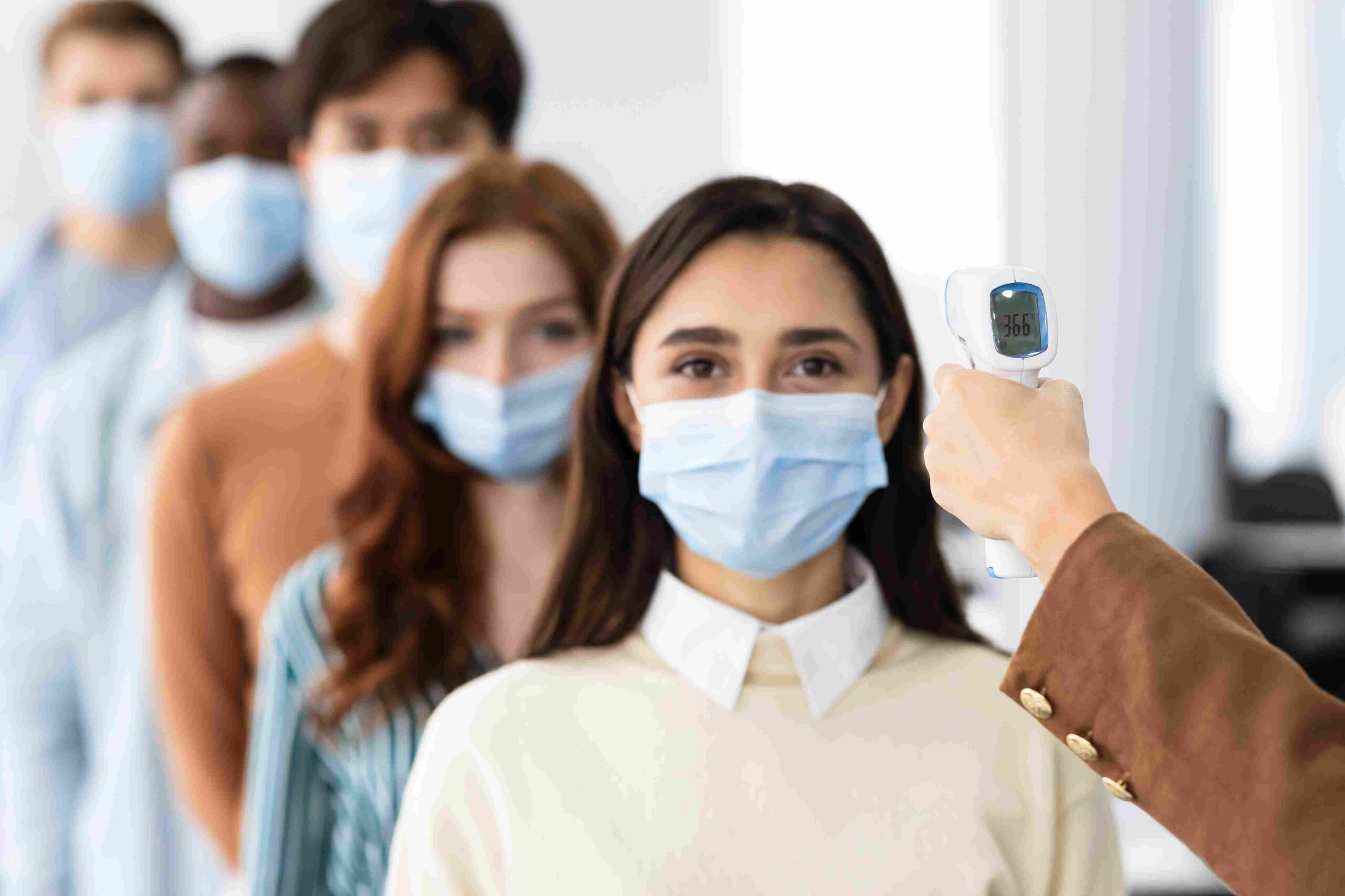 Studenti sa zaštitnim maskama stoje u redu dok im se meri temperatura