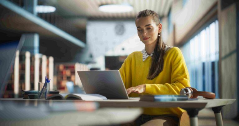 Studentkinja sedi za stolom i koristi laptop u prostoru za učenje